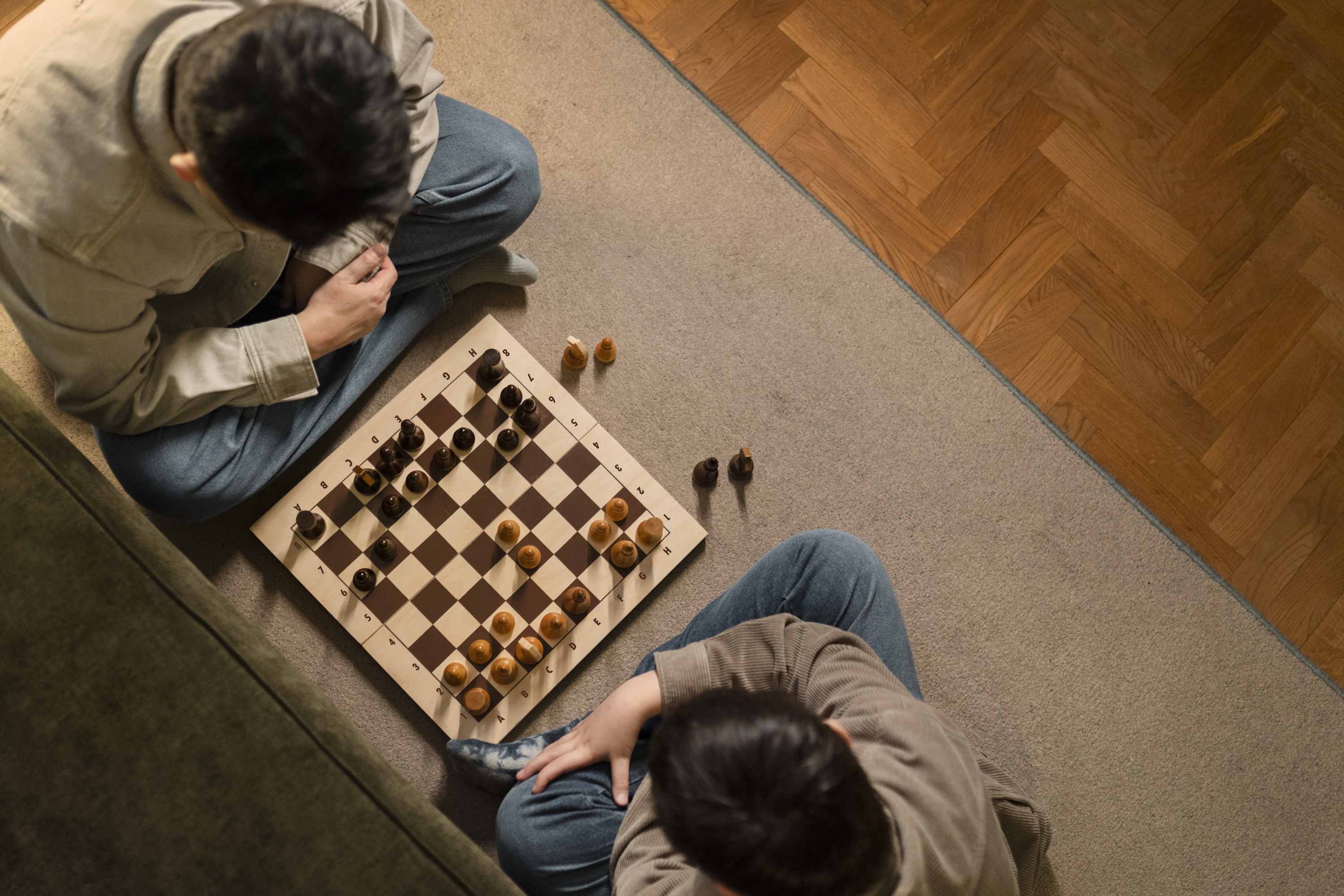Aerial Shot of Two Players Sitting and Playing Chess on a Board on a Carpet on a Wooden Floor in a Home