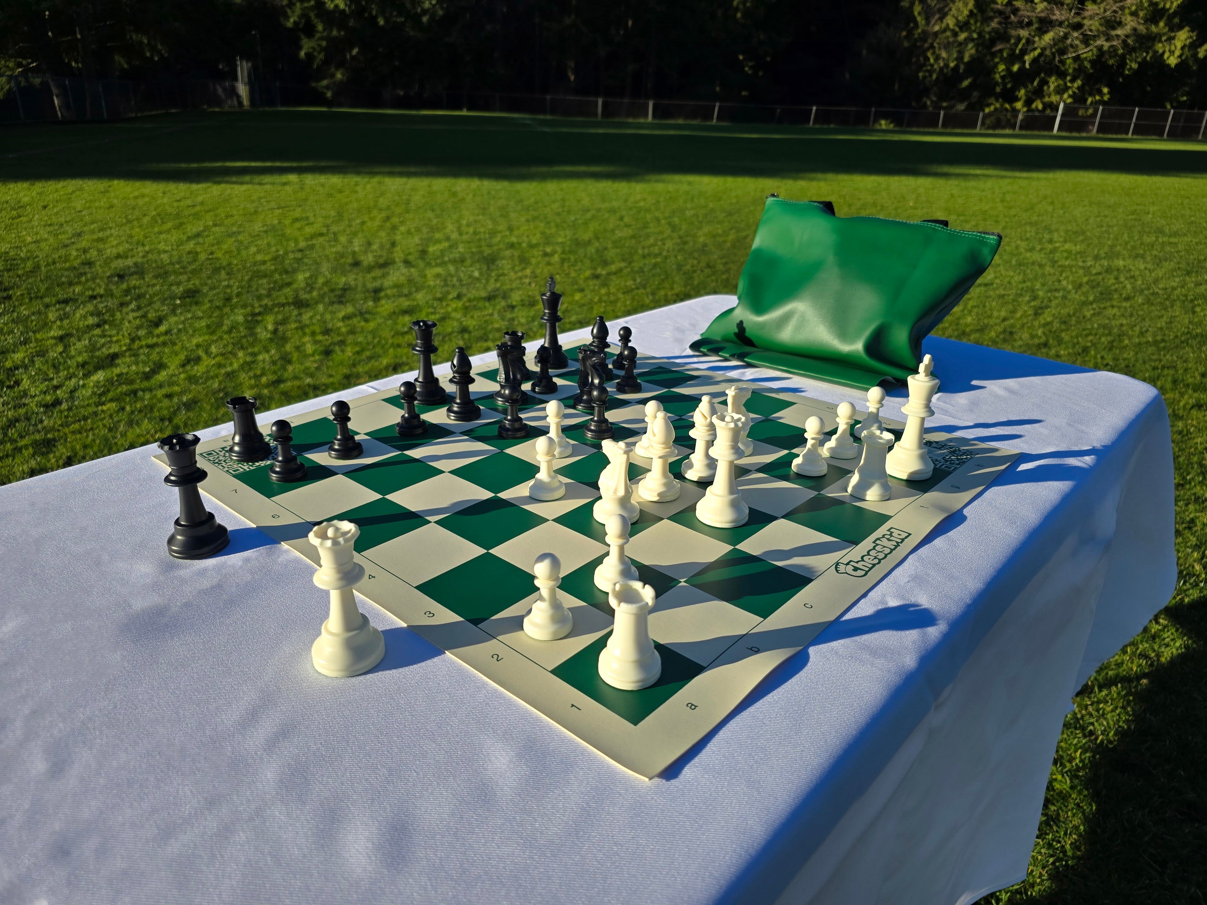 ChessKid Tote Chess Set with Vinyl Chess Board on White Cloth Table in Park (Under Shining Sun, Angled Shot A1)