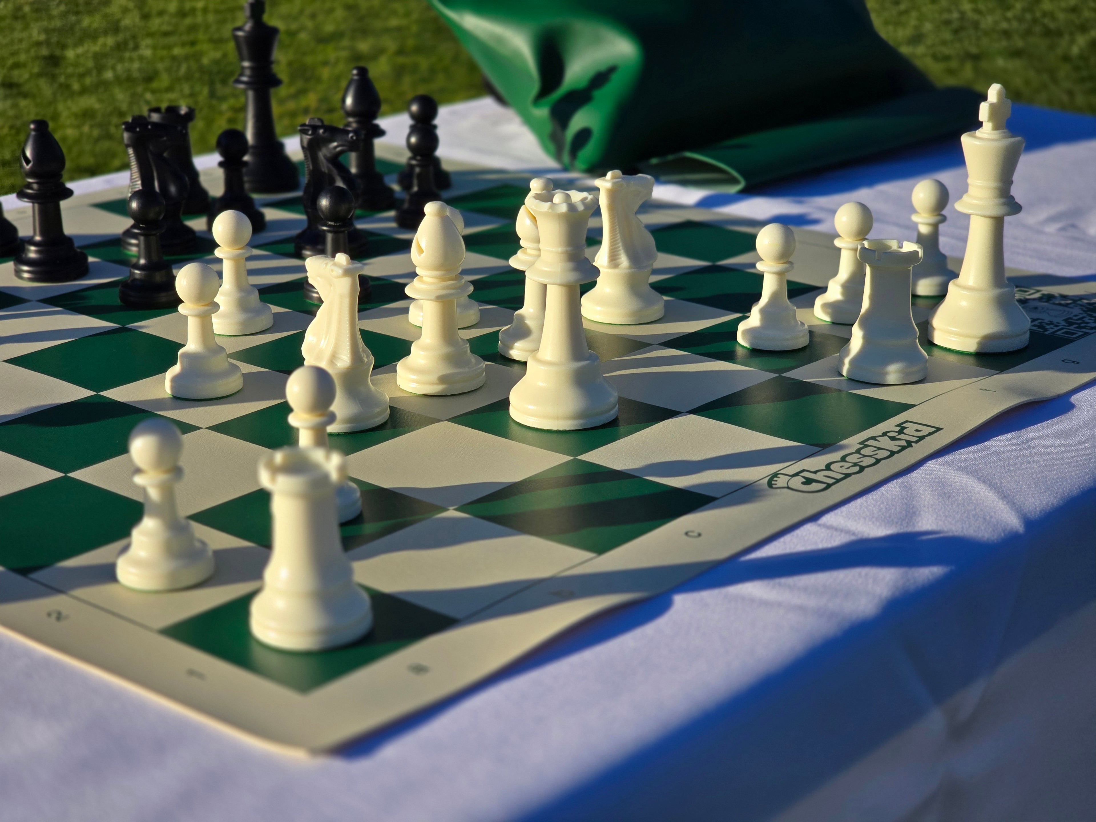 ChessKid Tote Chess Set with Vinyl Chess Board on White Cloth Table in Park (Close-Up Angle Featuring White Pieces)