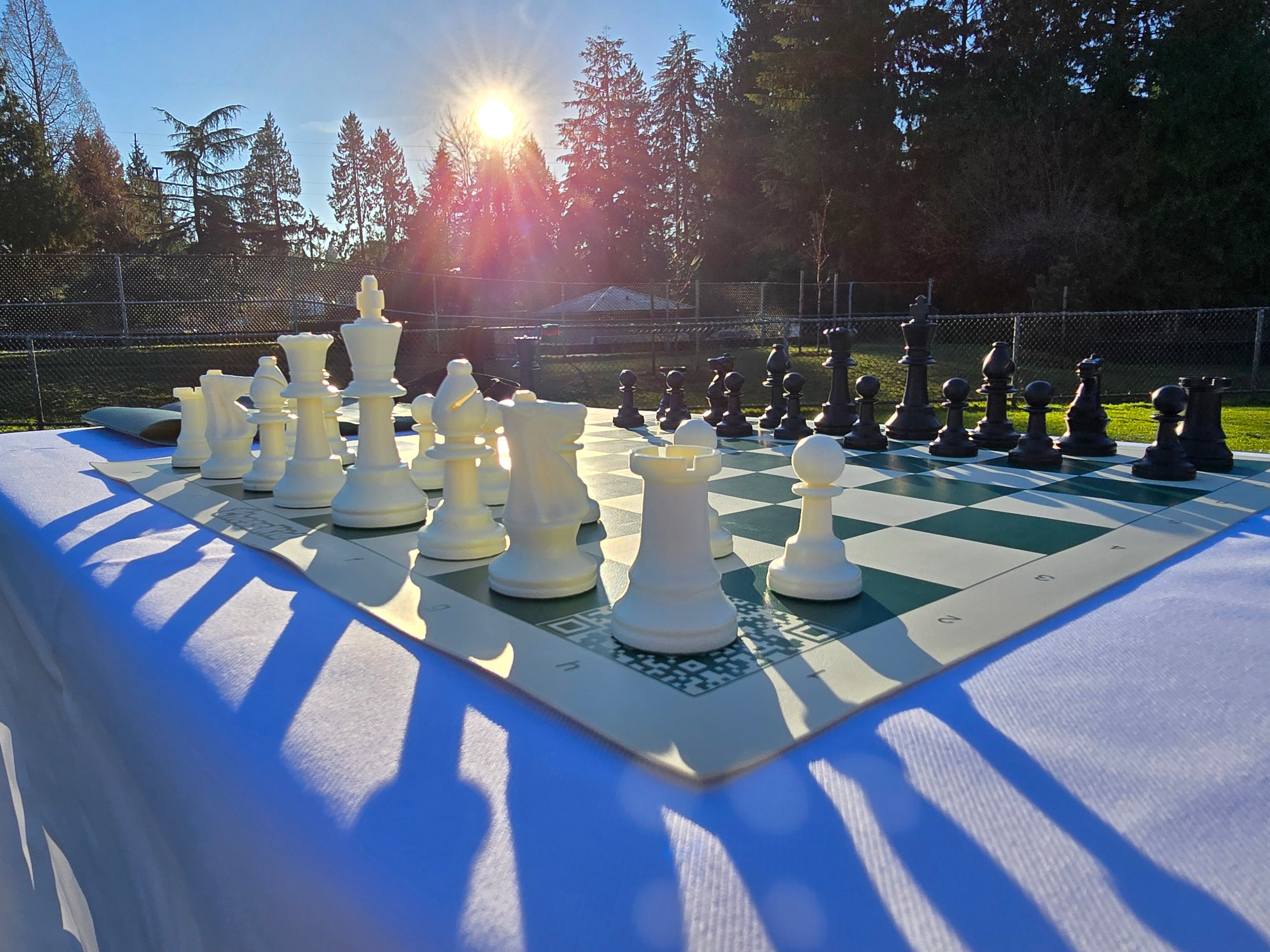 ChessKid Tote Chess Set with Vinyl Chess Board on White Cloth Table in Park (Shadowed Sun, Angled Shot, H1)