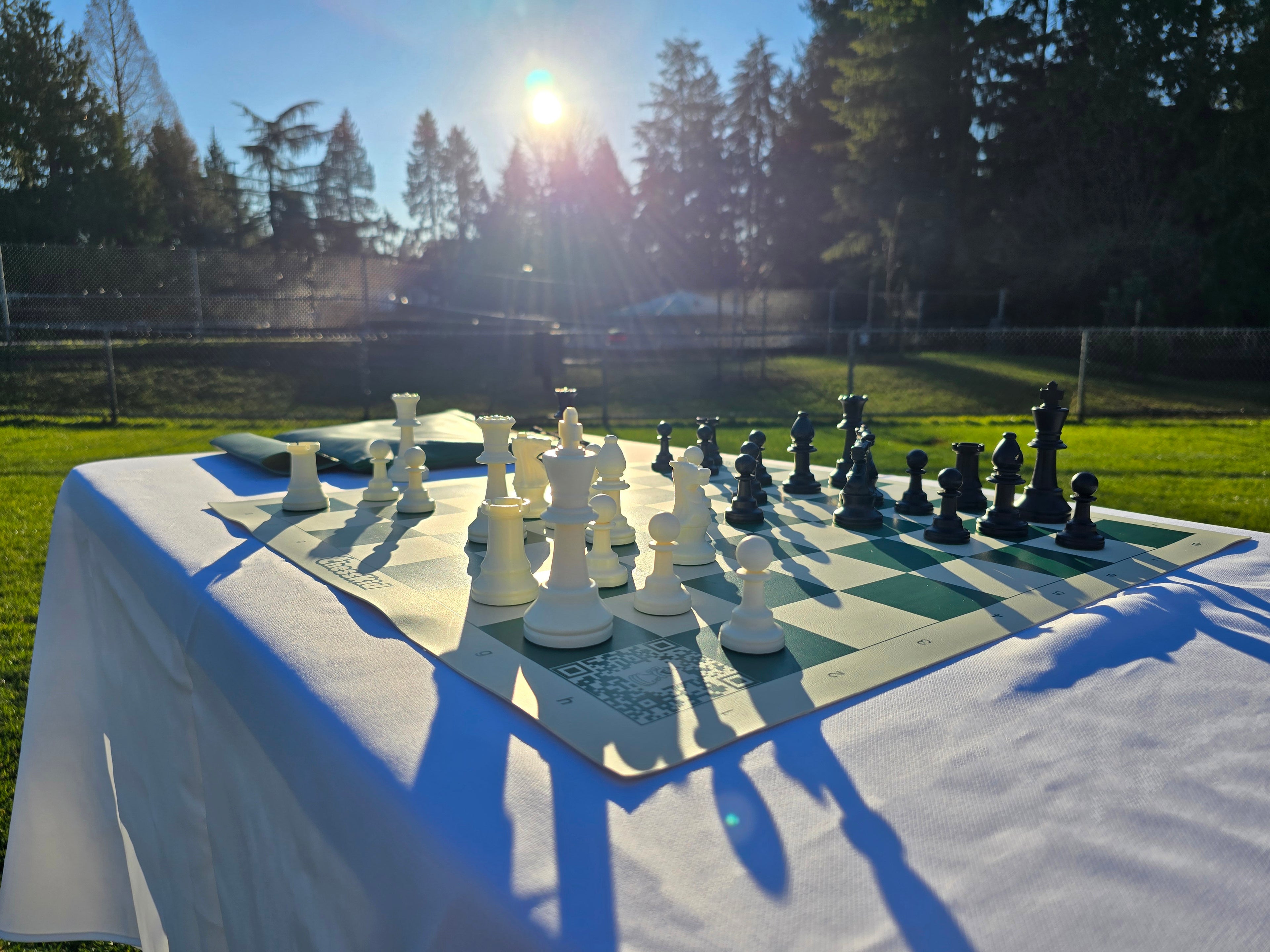 ChessKid Tote Chess Set with Vinyl Chess Board on White Cloth Table in Park (Under Shining Sun from H1 Angle)