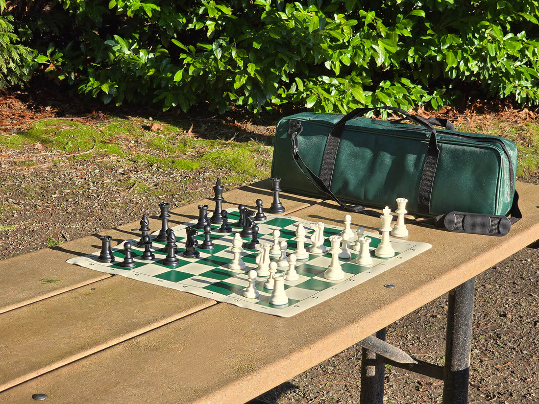 Chess set with pieces on a board outdoors, next to a green carrying case.