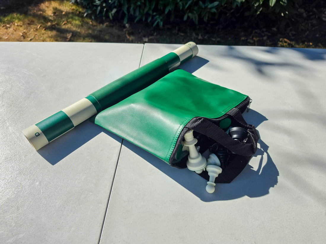 Unzipped green tote bag showing plastic chess pieces stored inside alongside a rolled green vinyl board.