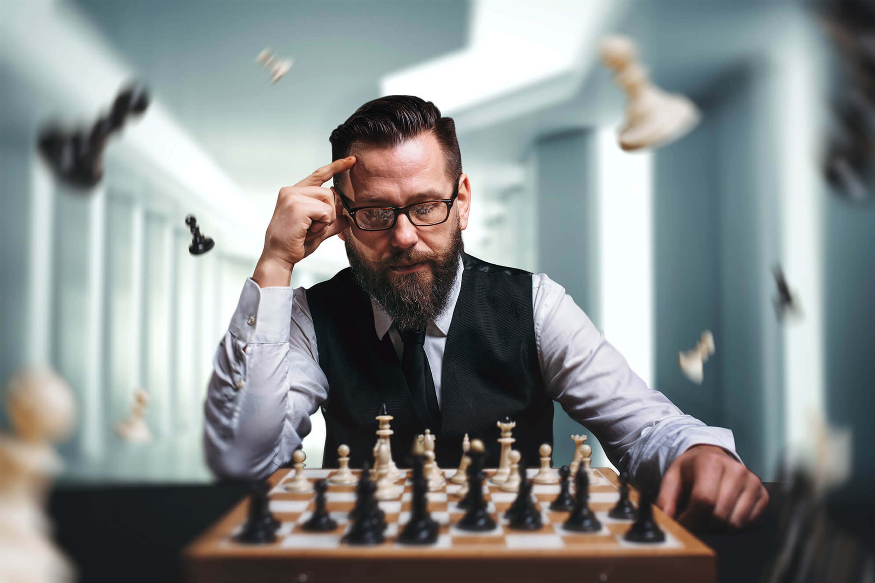 Man with Beard and Glasses Concentrating Intently on a Wooden Chess Board with Pieces Flying Around Him