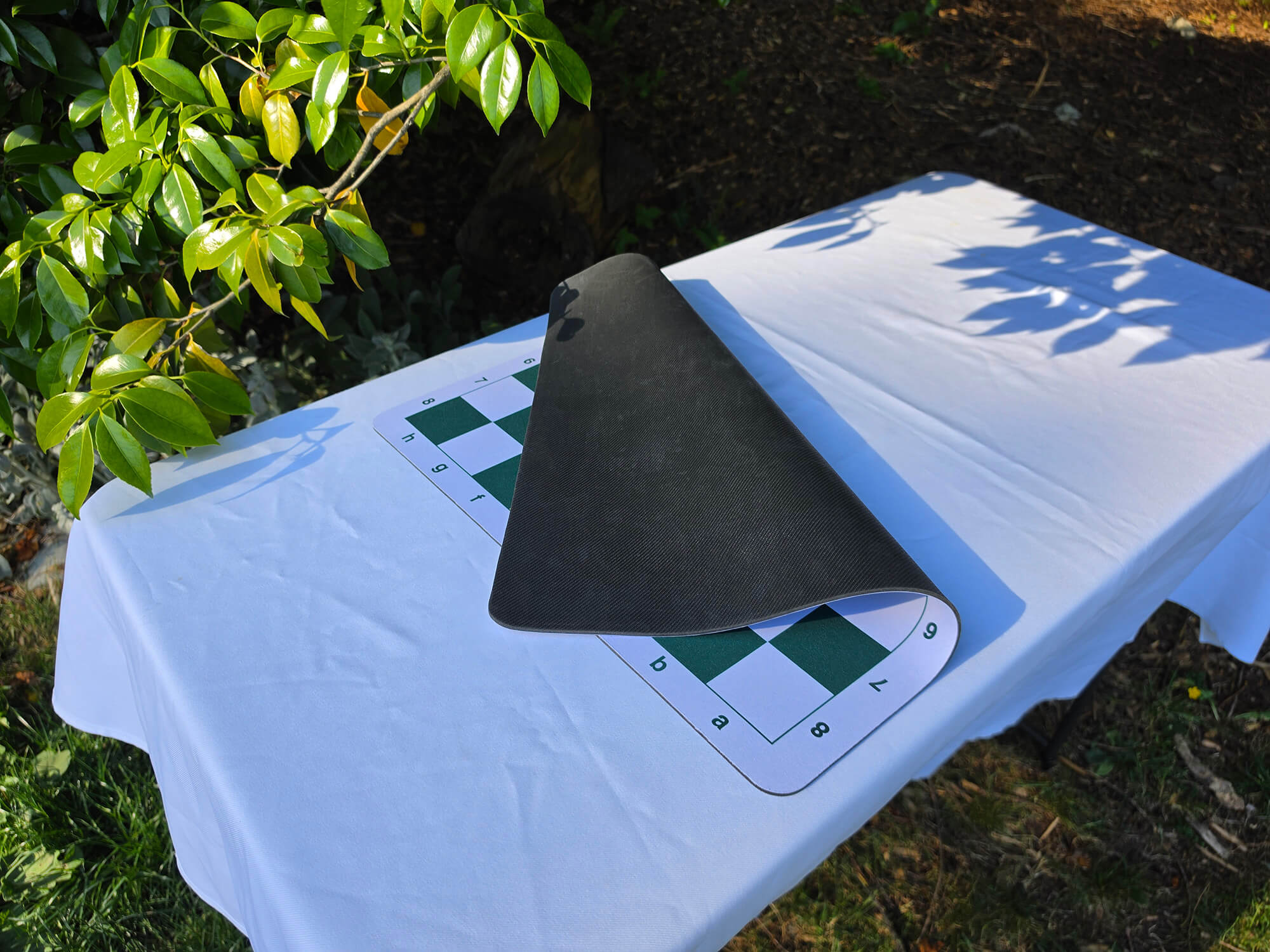 A green and white mousepad chess board partially folded over to show its flexible design and thick black rubber backing.