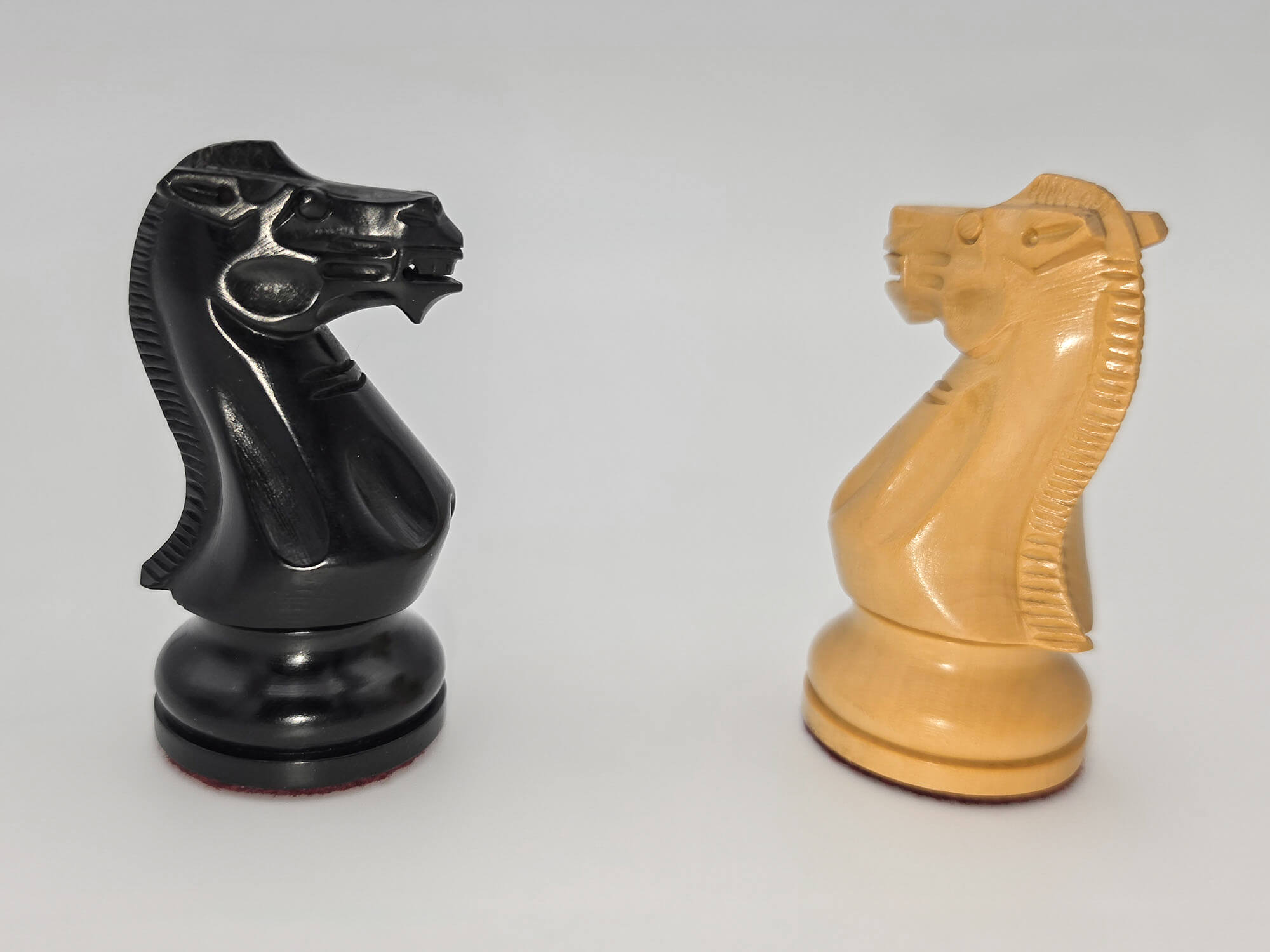 Black and natural wood Judit Polgar chess set knights standing side by side against a white background.
