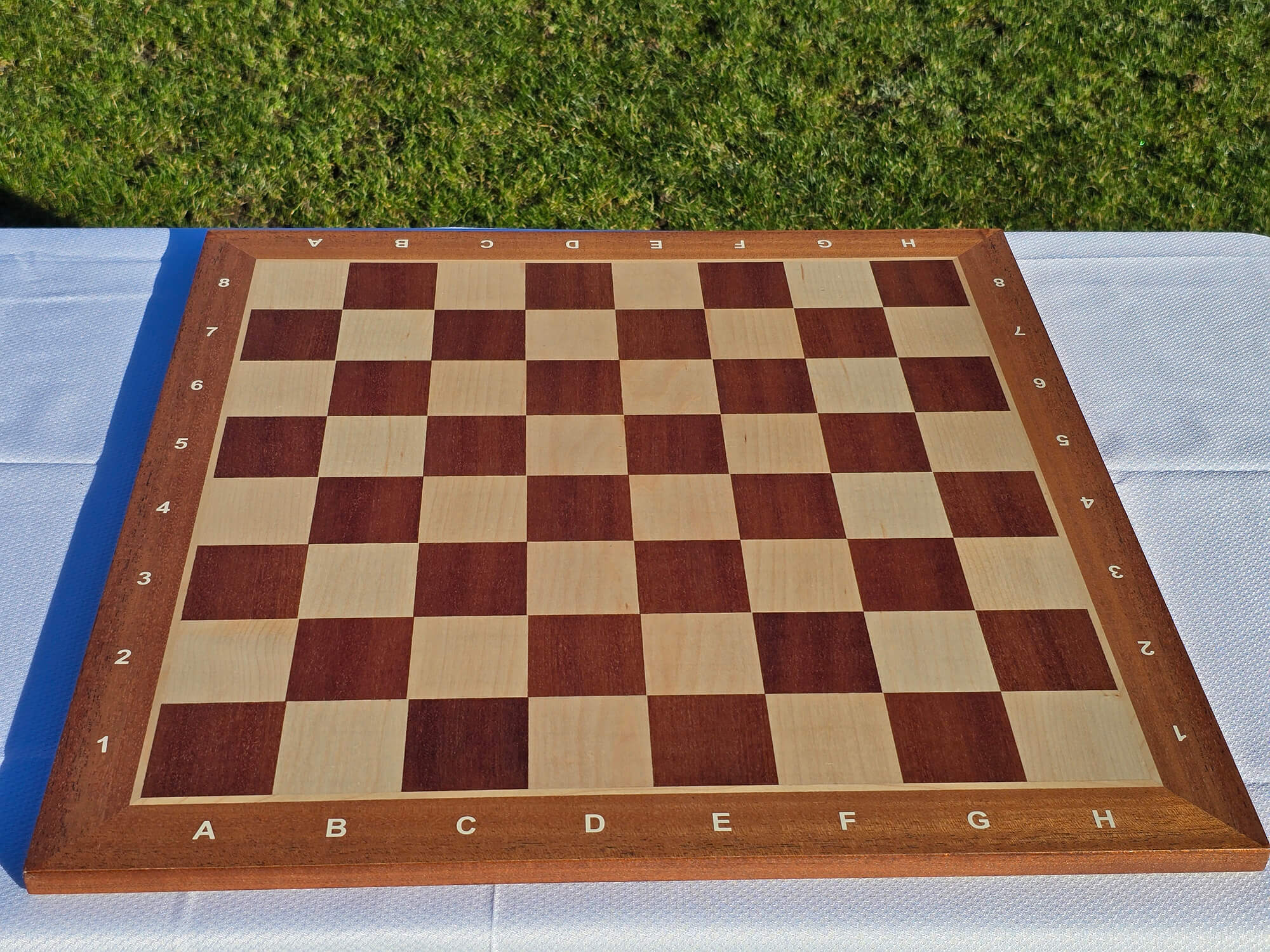 Top-down view of a high-quality mahogany and maple wooden chess board with professional algebraic notation.