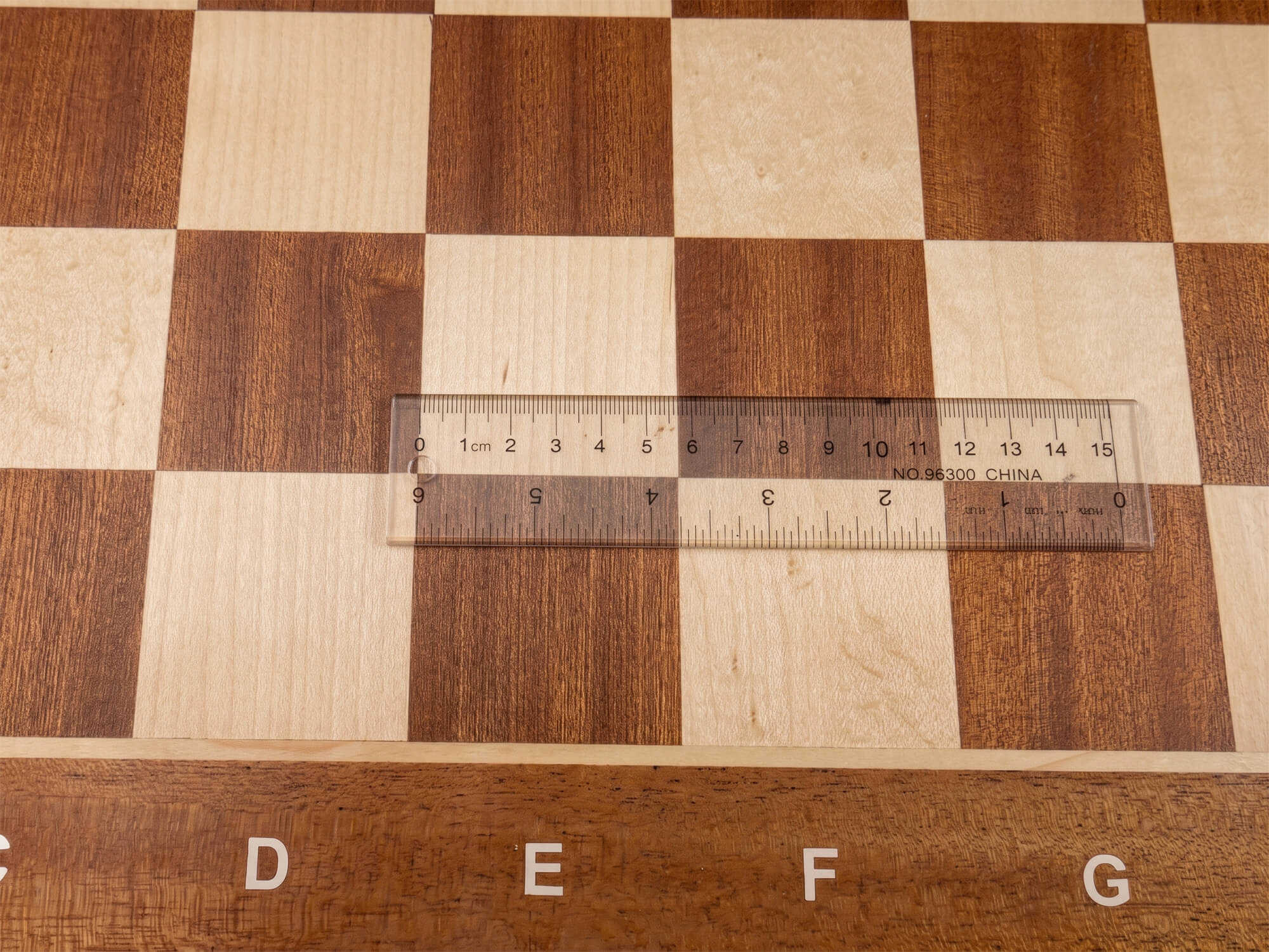 Close-up top view of the Monarch chess board with a transparent ruler placed across a square, confirming the precise 57mm regulation square measurement.