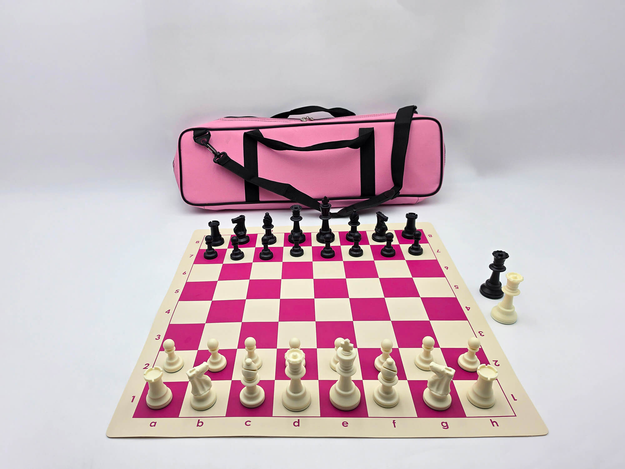 Pink deluxe chess set with black and white Staunton pieces set up on a pink and white vinyl board with extra queens and a matching pink bag behind it.