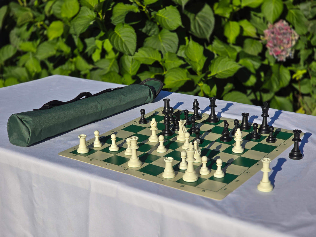 Tournament weighted chess set with green roll-up vinyl board and matching green quiver-style carrying bag with shoulder strap, displayed outdoors on a white table.