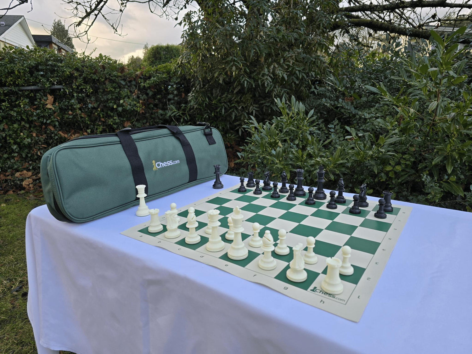 Chess.com Chess Set with Vinyl Chess Board and Deluxe Bag on White Table in Garden Setting (Angled H1)