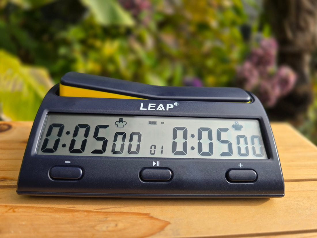 Leap KK9909 Chess Clock on Wooden Board with pink flowers and bush in background.