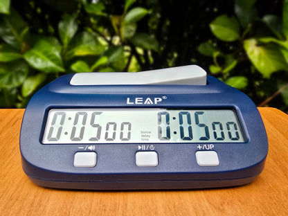 Leap PQ9923 Chess Clock on Wood Base Outside with Blurred Green Hedge with Time On.