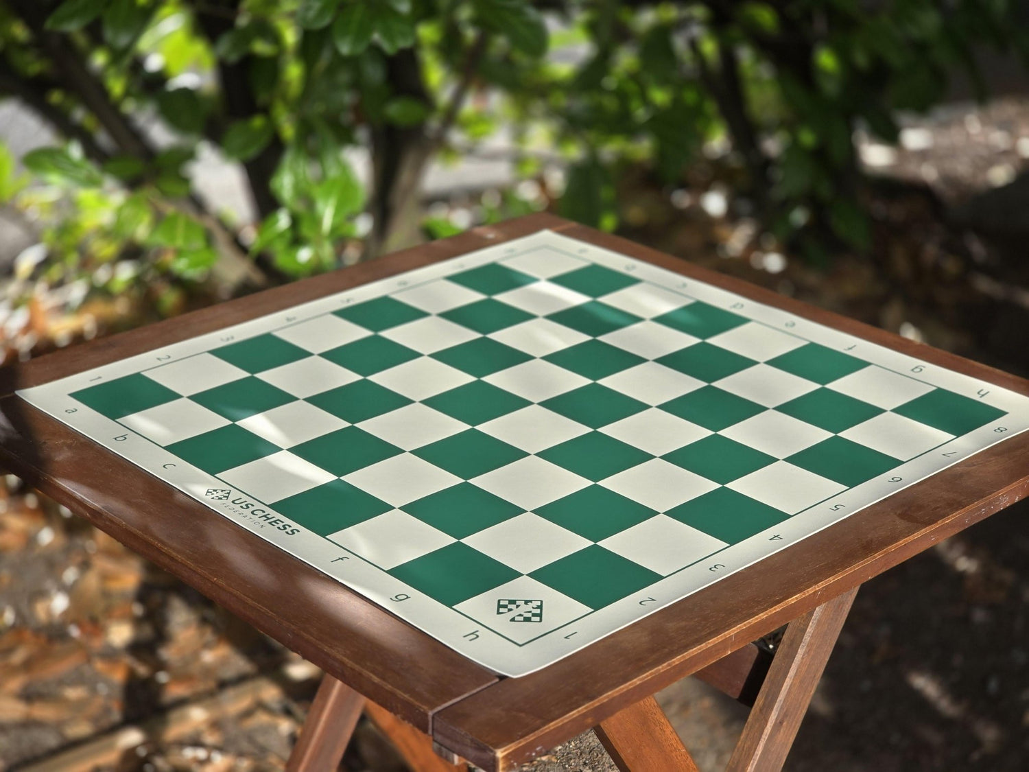 US Chess Federation Vinyl Chess Board on a Patio Table with a Hedge in the Background