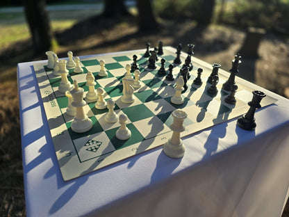 US Chess Federation Tournament Chess Set with USCF Vinyl Chess Board on a White Cloth Table in a Park at Twilight with Sunlight Glinting Off It