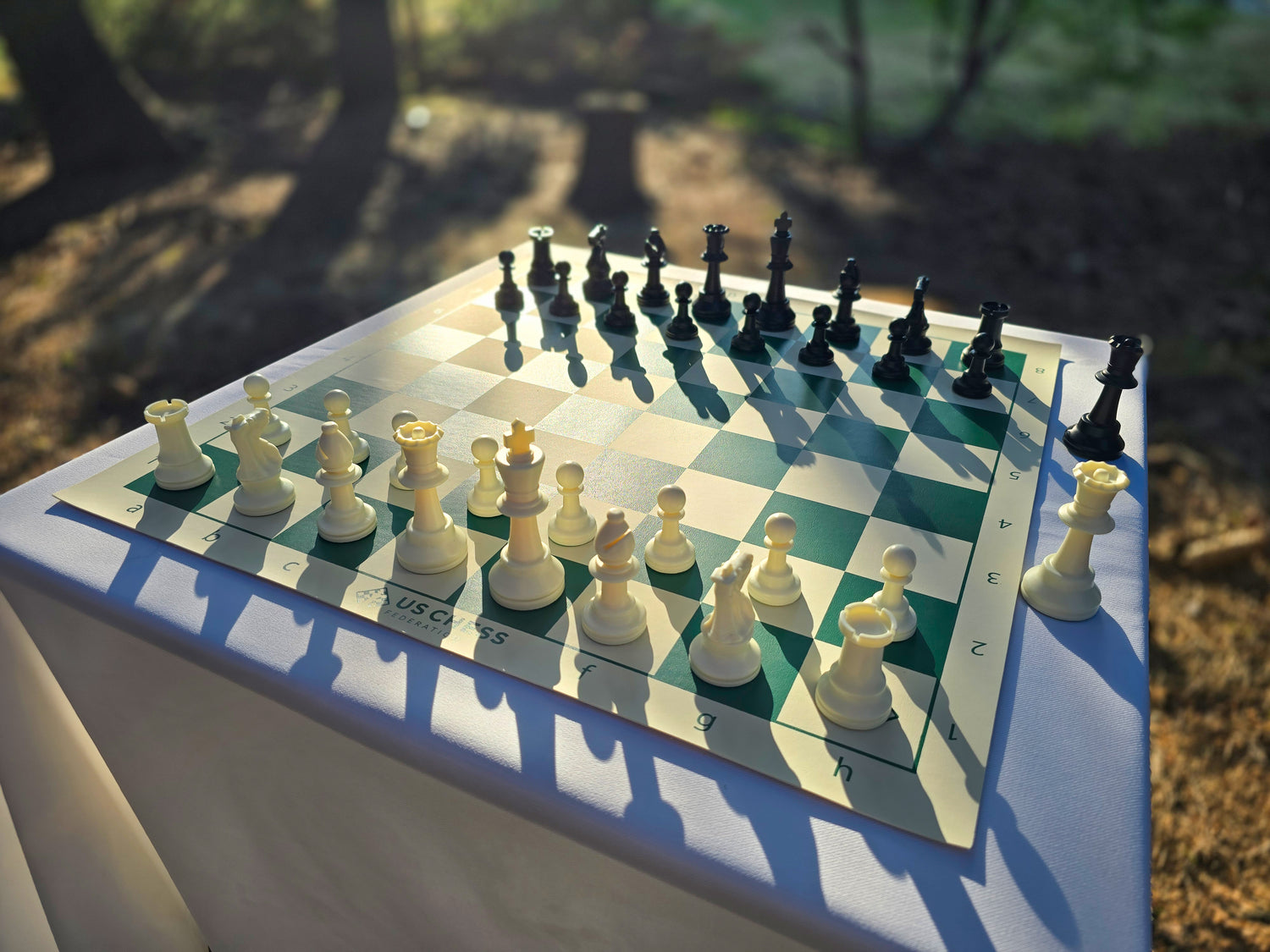 US Chess Federation Tournament Chess Set on USCF Vinyl Chess Board at Twilight with Sunlight Glinting Off the Pieces and Board