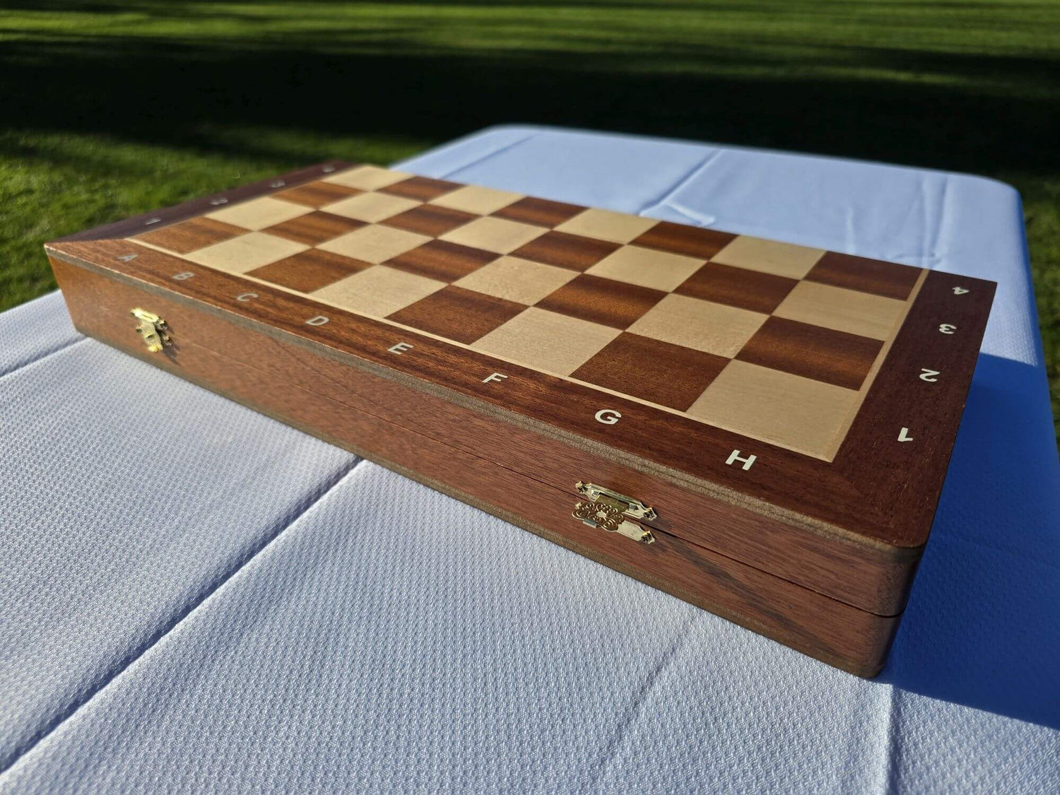 The closed wooden storage box of the Aristocrat folding wooden chess set on a white tablecloth outdoors.