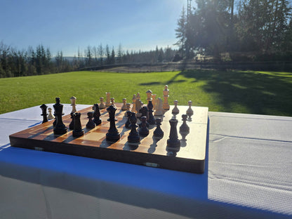 Aristocrat folding wooden chess set beautifully set up on a park table with a scenic green grass field backdrop.