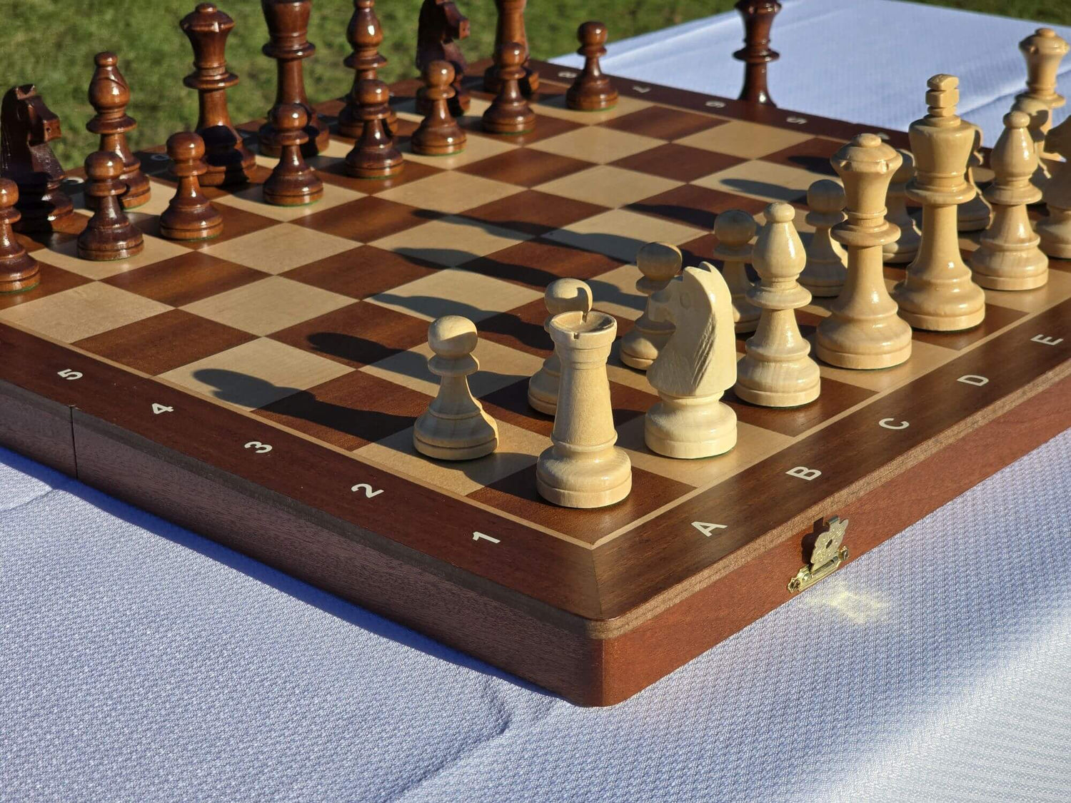 Complete Aristocrat folding wooden chess set fully set up for a game on a white tablecloth outdoors.