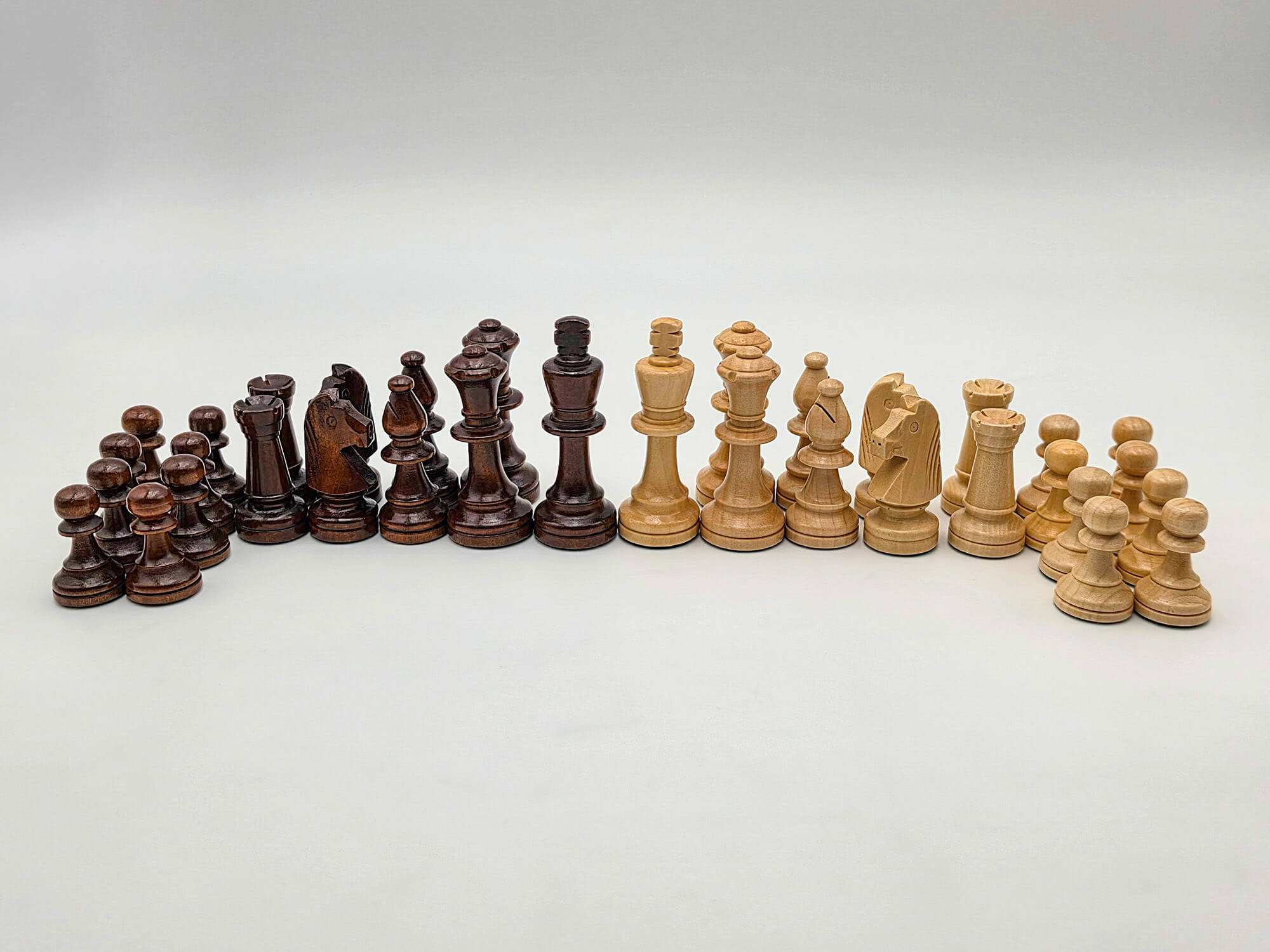 A full line-up of the light and dark wooden chess pieces from the Aristocrat set arranged inside a studio lightbox.