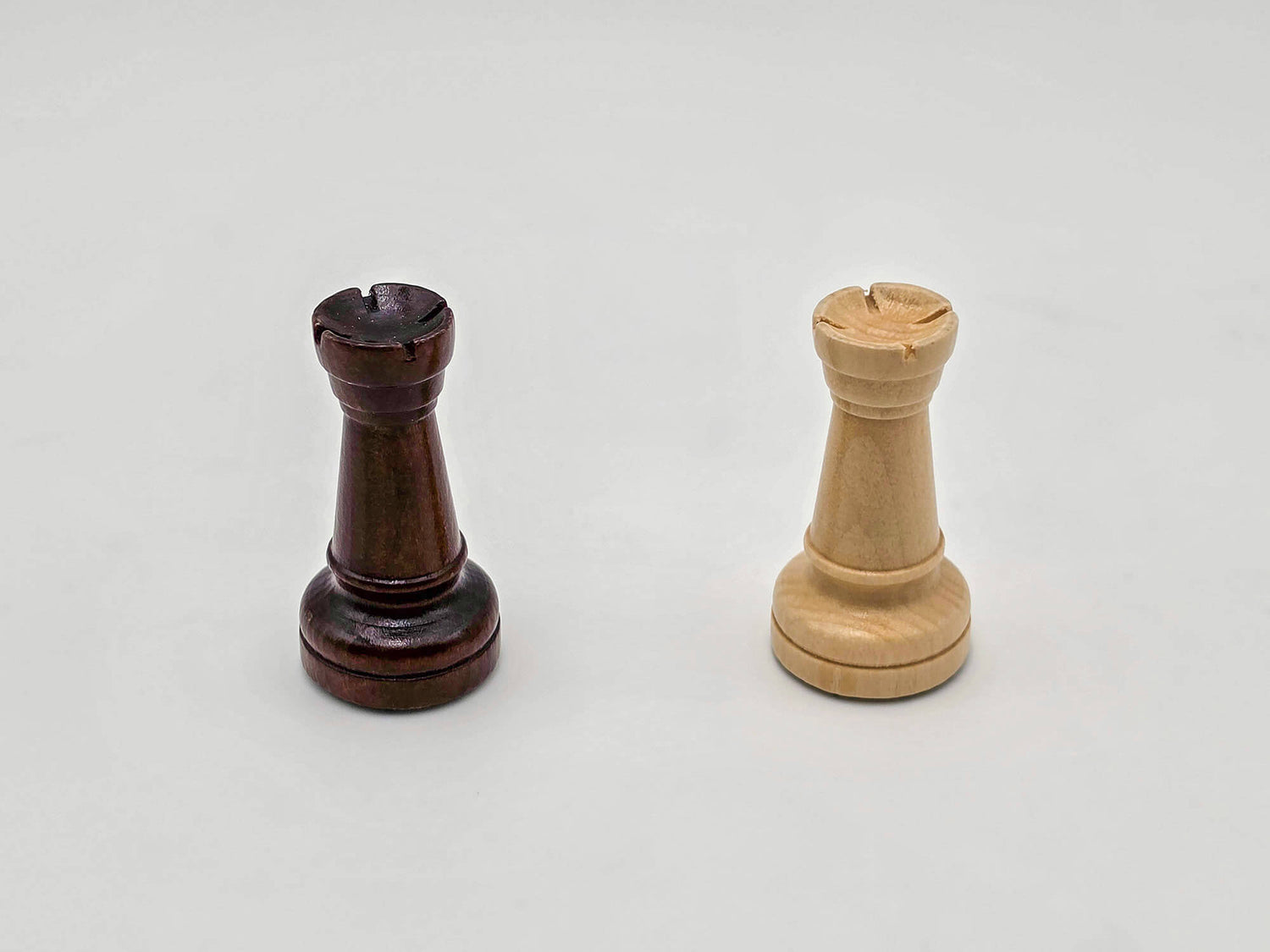 Side-by-side white background photo of the dark and light wooden rook pieces from the Aristocrat chess set.