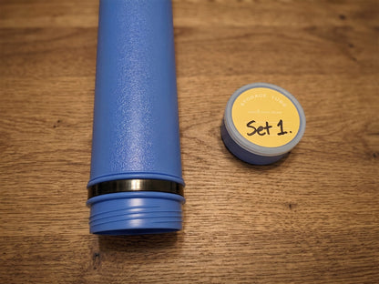 Blue Sentry telescopic chess tube body with a detached cap. The cap has a yellow circular label with handwritten black text that reads &