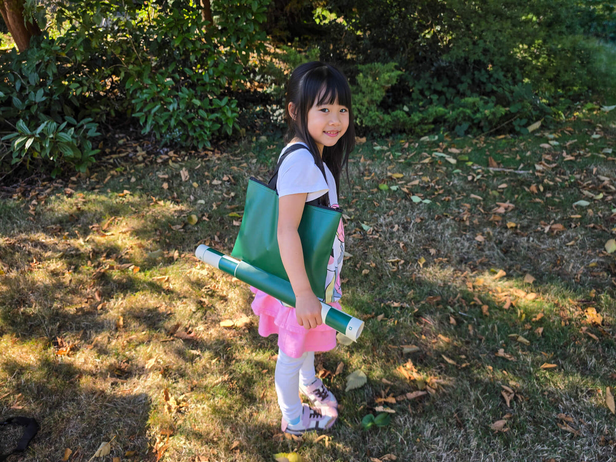 Young girl carrying the portable green Campaigner Tournament chess tote bag and rolled board over her shoulder outdoors.