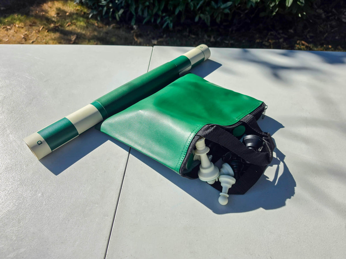 Unzipped green tote bag showing plastic chess pieces stored inside alongside a rolled green vinyl board.