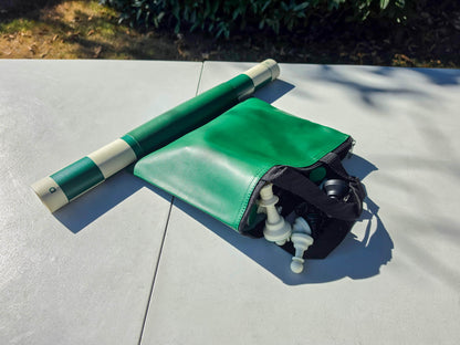 Unzipped green tote bag showing plastic chess pieces stored inside alongside a rolled green vinyl board.