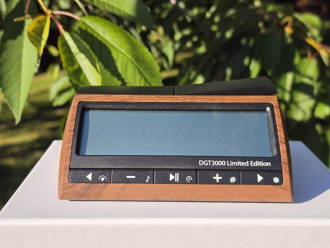 Front view of the DGT 3000 Limited Edition digital chess clock with a wood-grain finish, displayed outdoors against a natural green foliage background.