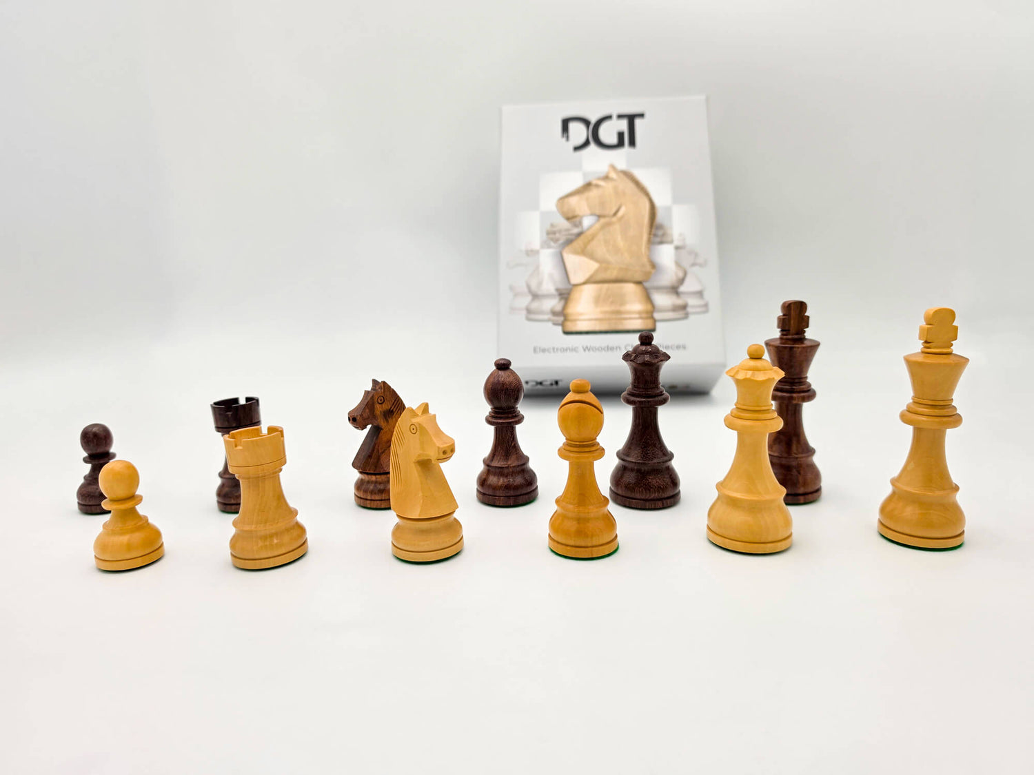Complete collection of handcrafted wooden DGT Timeless chess pieces laid out with the product packaging box in a studio setting.