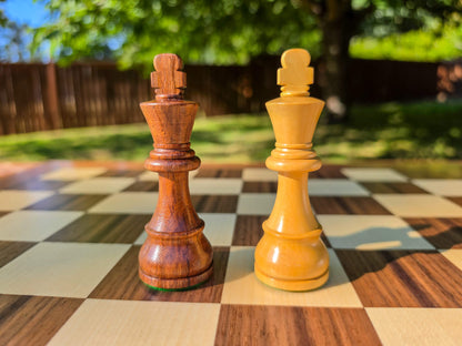 Close-up view of the handcrafted dark wood and light wood King pieces from the DGT Timeless electronic chess set, set on a wooden chess board outdoors with a nature background.
