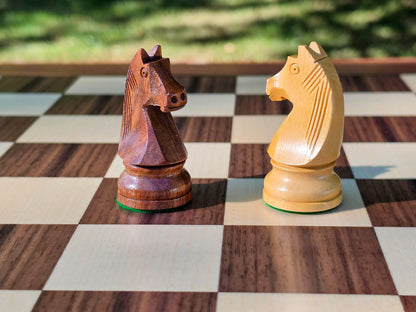Detailed close-up of the handcrafted dark and light wooden Knight pieces from the DGT Timeless Staunton chess set with a nature background.