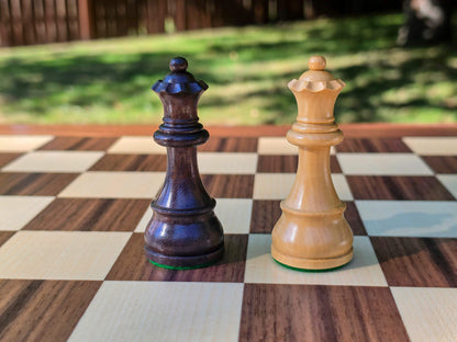 Side-by-side close-up photo of the dark brown and light wooden Queen pieces from the DGT Timeless electronic chess set on an e-board with a nature background.