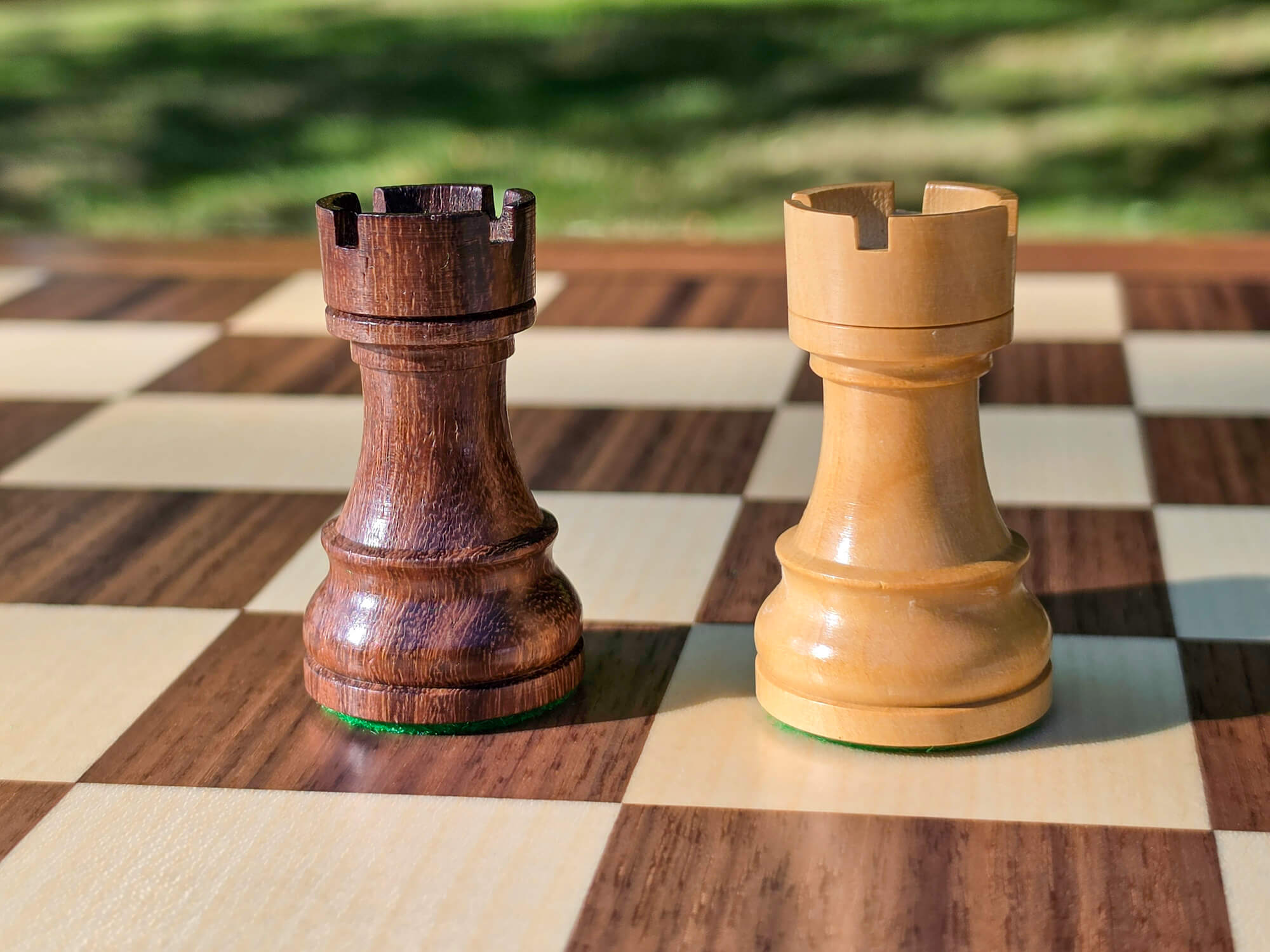 Dark wood and light wood Rook pieces from the DGT Timeless electronic chess set shown in detail on a board square with a nature background.