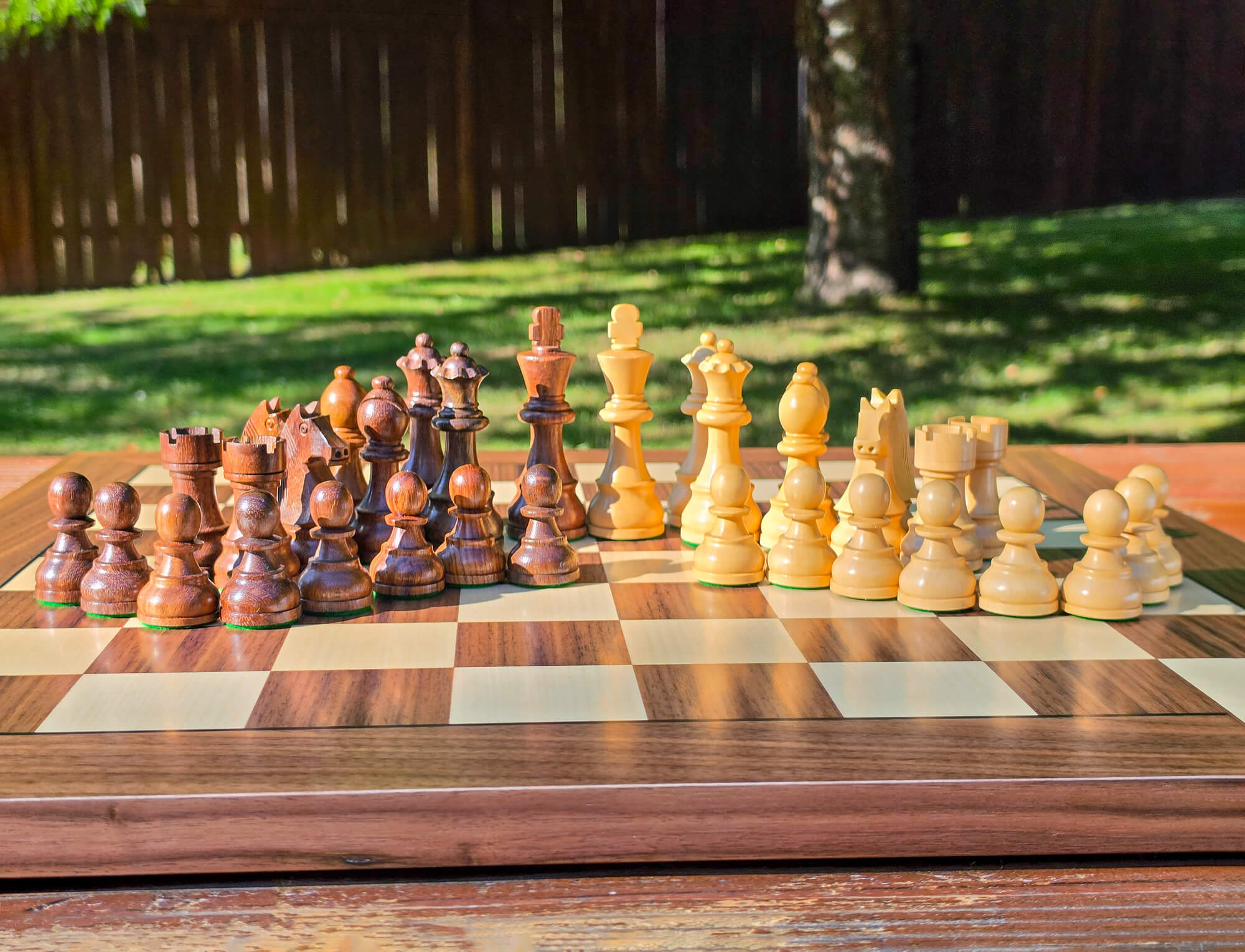 Complete set of DGT Timeless wooden chess pieces arranged in starting position on an e-board placed on a wooden picnic table outside with a nature background.