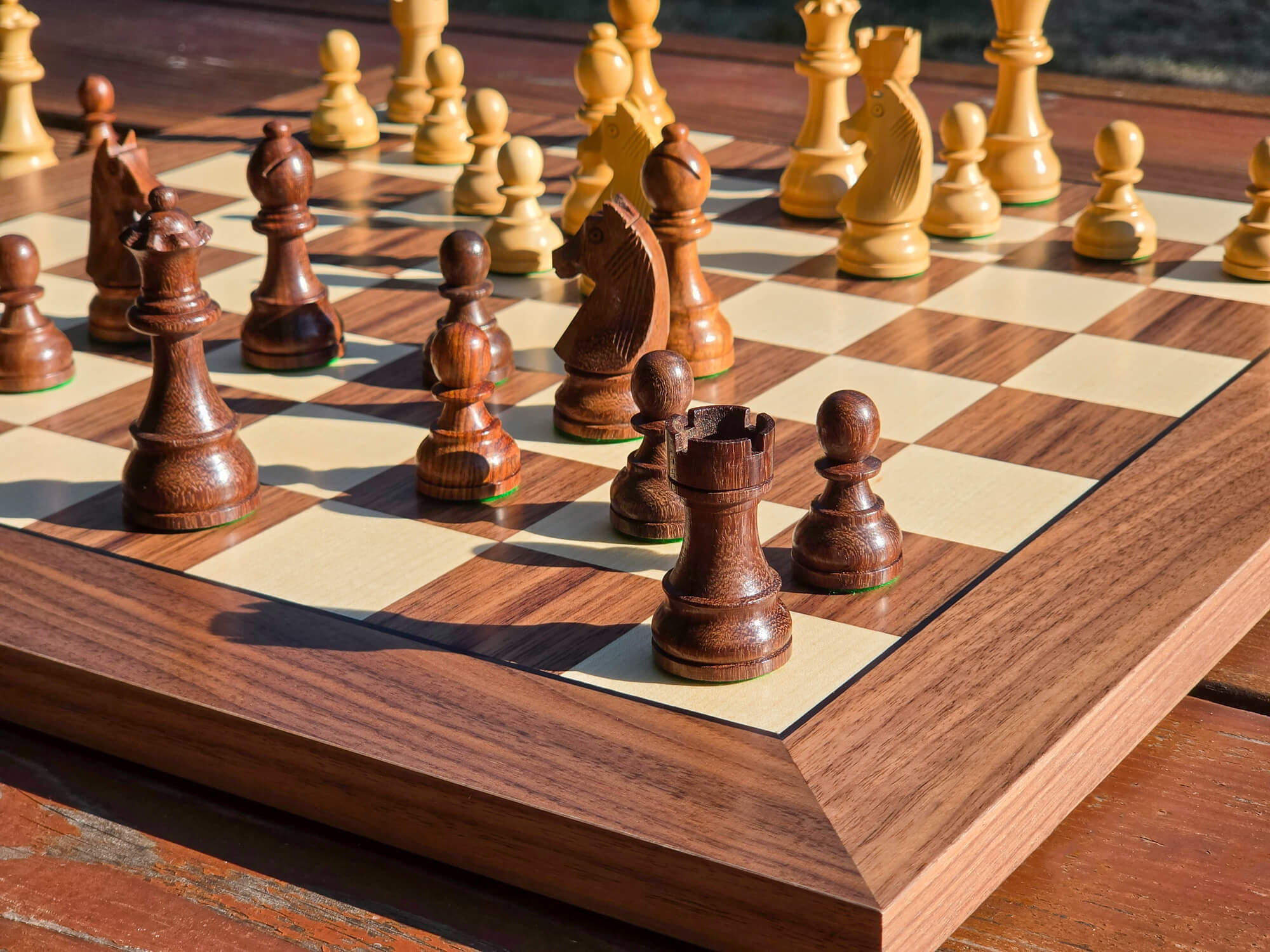 Low-angle close-up view focusing on the dark pieces of the DGT Timeless electronic chess set on a DGT Walnut e-board outdoors with a nature background.