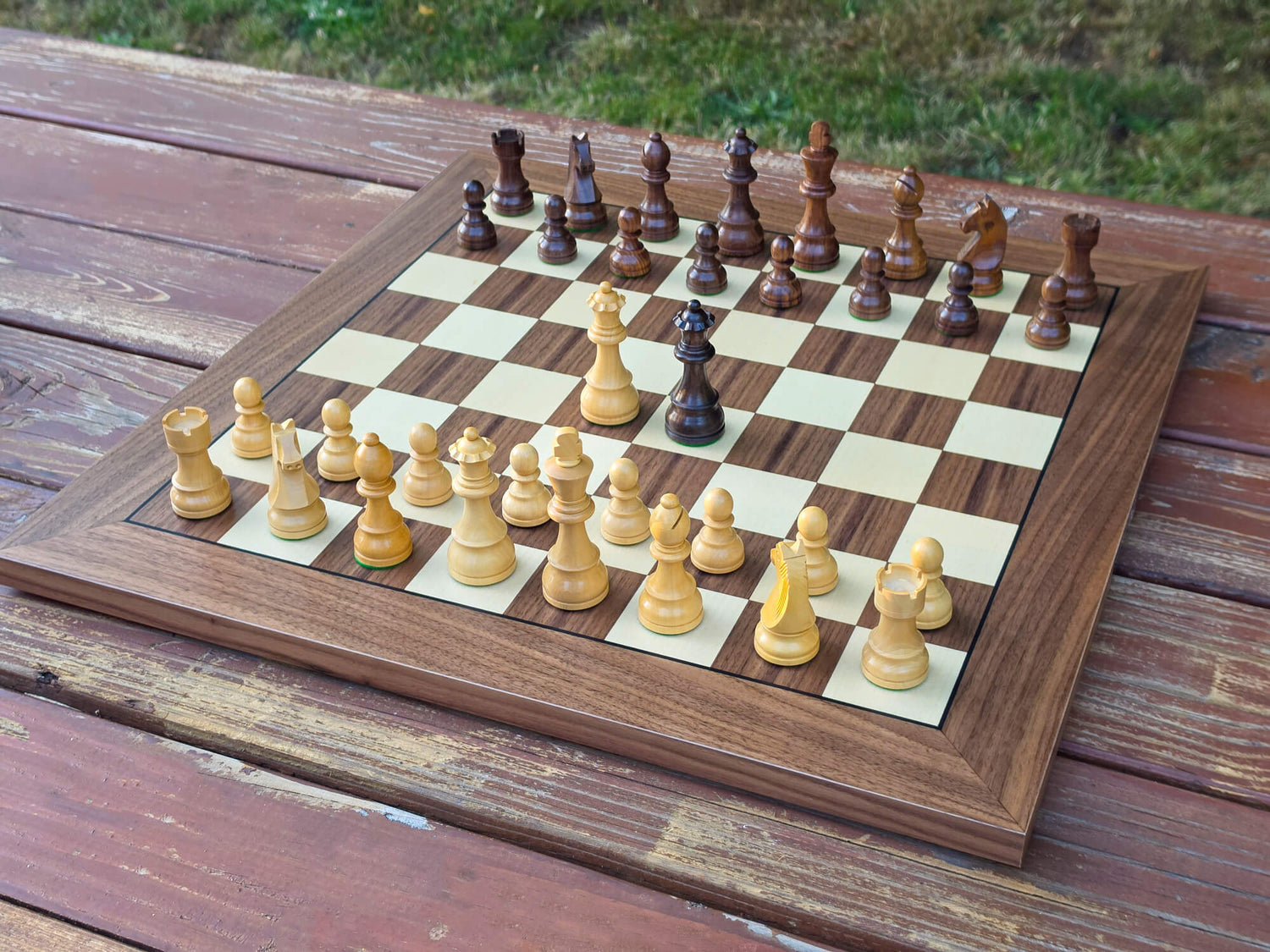 Overhead top-down view showing the full setup of DGT Timeless chess pieces on a DGT Walnut wooden chess e-board outdoors with a nature background.