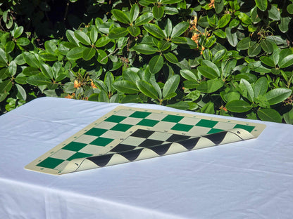 Folded double-sided silicone chess board showing both green and black playing surfaces on an outdoor table with a nature background.