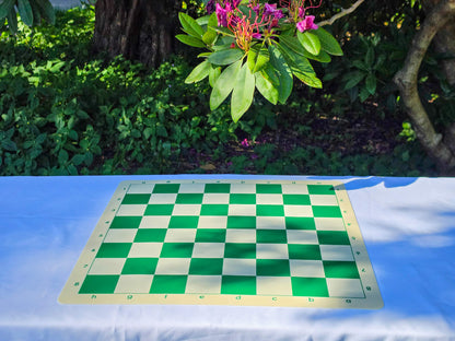 Double-sided silicone chess board laying flat on its green and white side on an outdoor table with a nature background.
