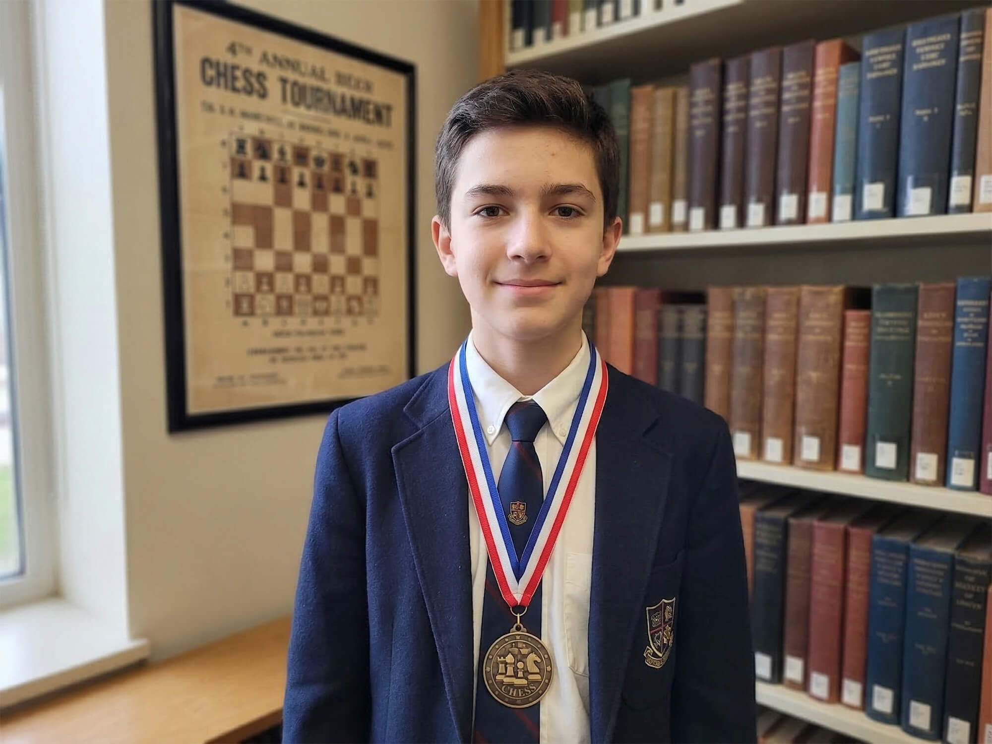 A young boy in a blazer proudly wearing the Classic Emblem gold medal around his neck at a chess competition.