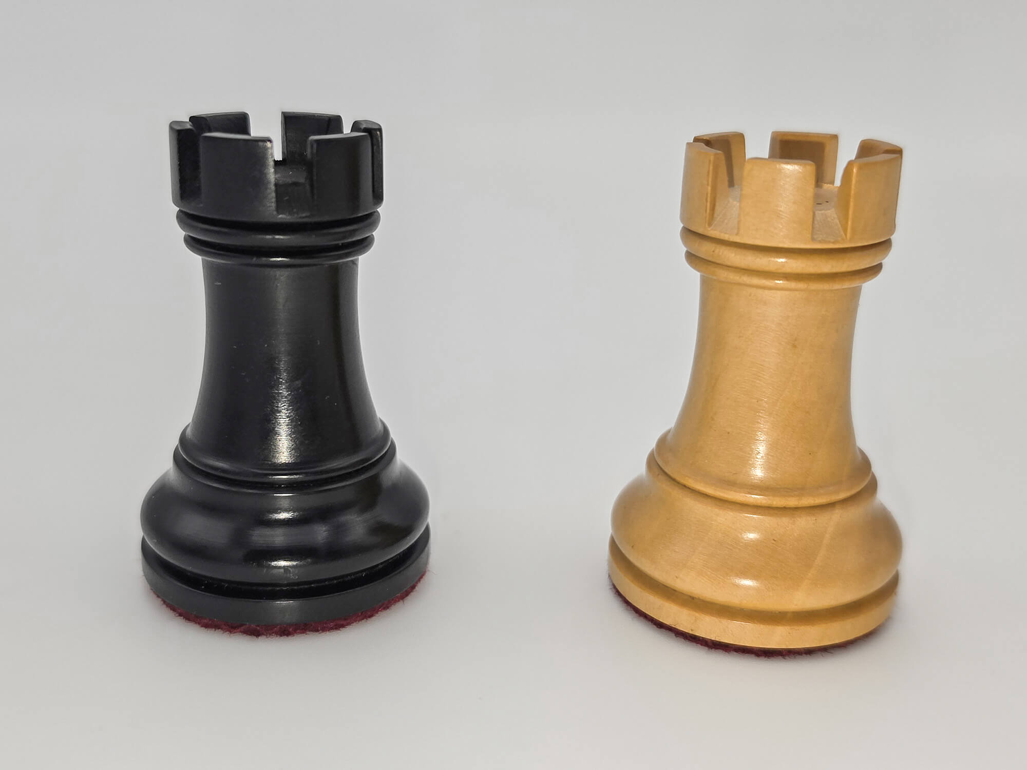 Black and natural wood Judit Polgar chess set rooks standing side by side against a white background.