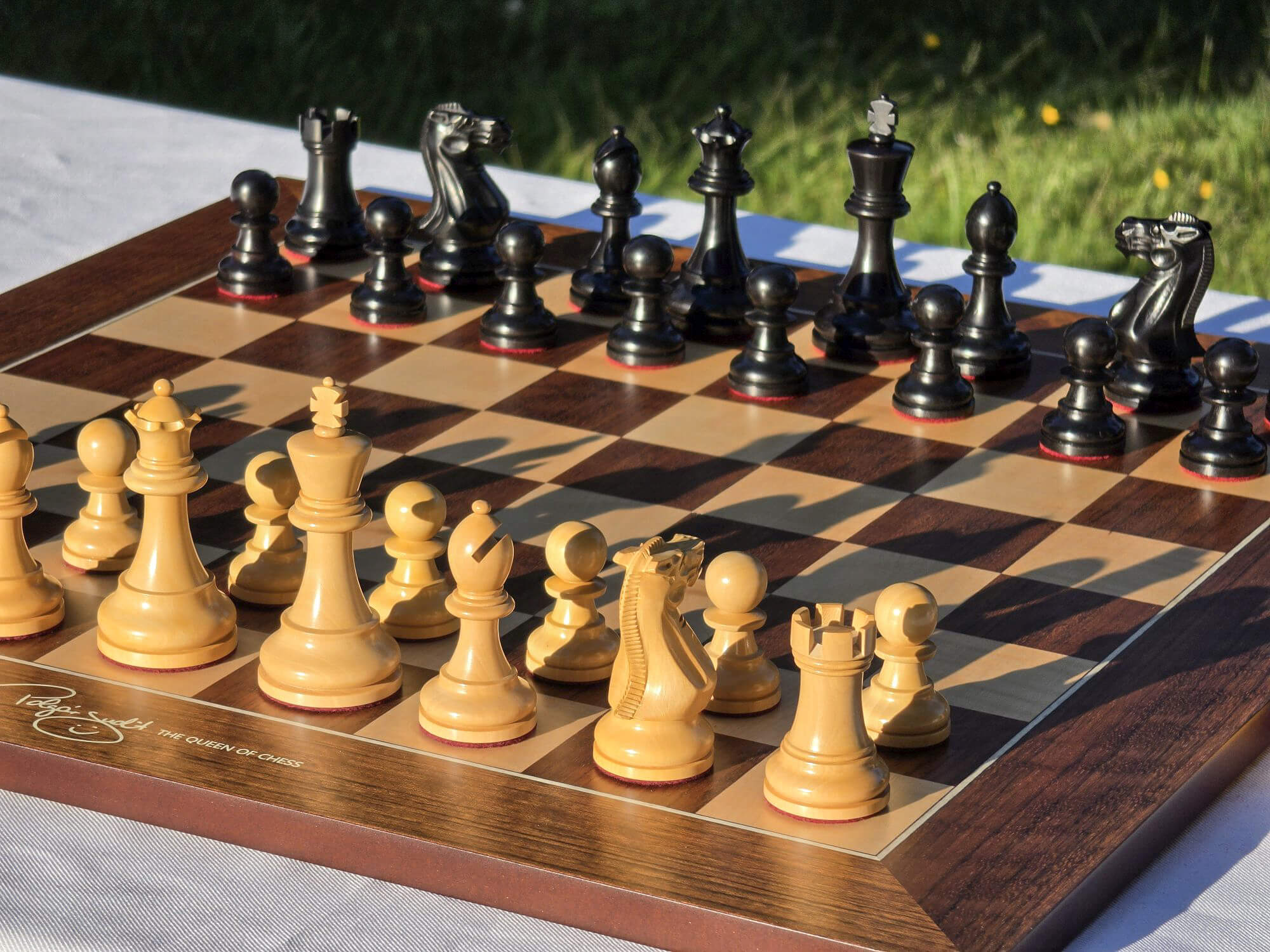 Angled outdoor view of a full set of Judit Polgar wooden chess pieces set up on the board.