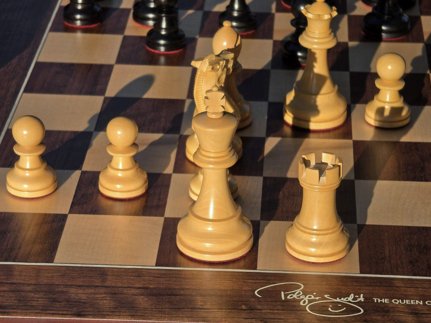 Close-up of the natural wood king and rook pieces on a Judit Polgar chessboard under natural lighting.