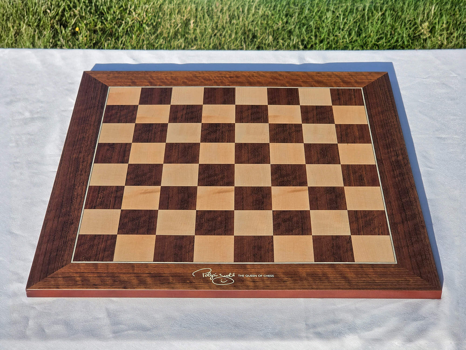 High-angle shot of the official Judit Polgar wooden chessboard set up on a white table.