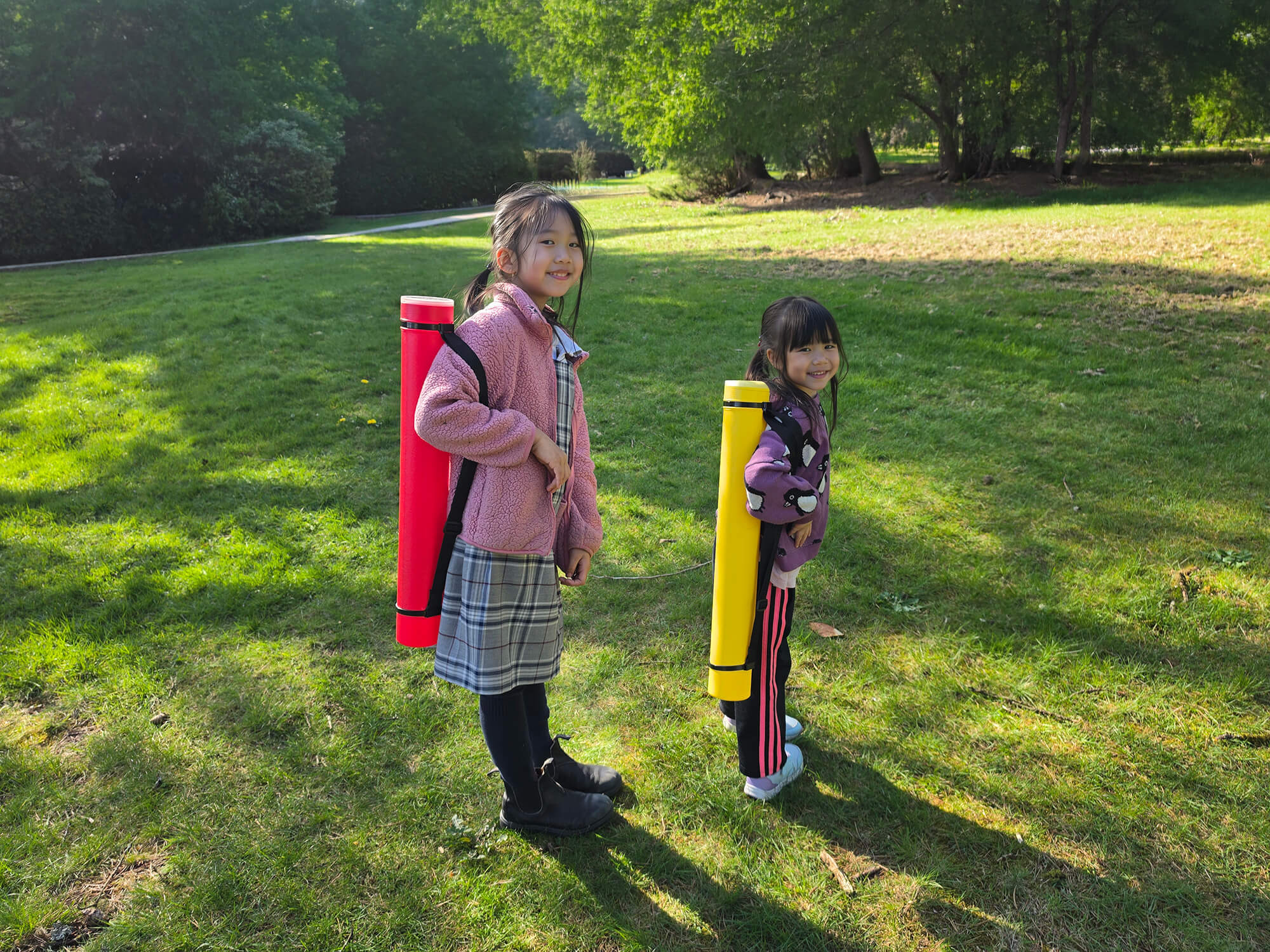 Two young girls carrying red and yellow Sentry telescopic chess tubes using the integrated shoulder straps.