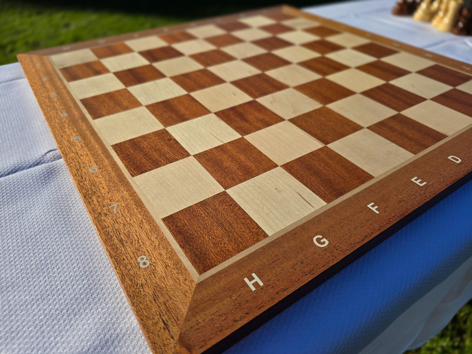 Close-up detail of the mahogany chess board corner focusing on the H8 square and smooth finish.