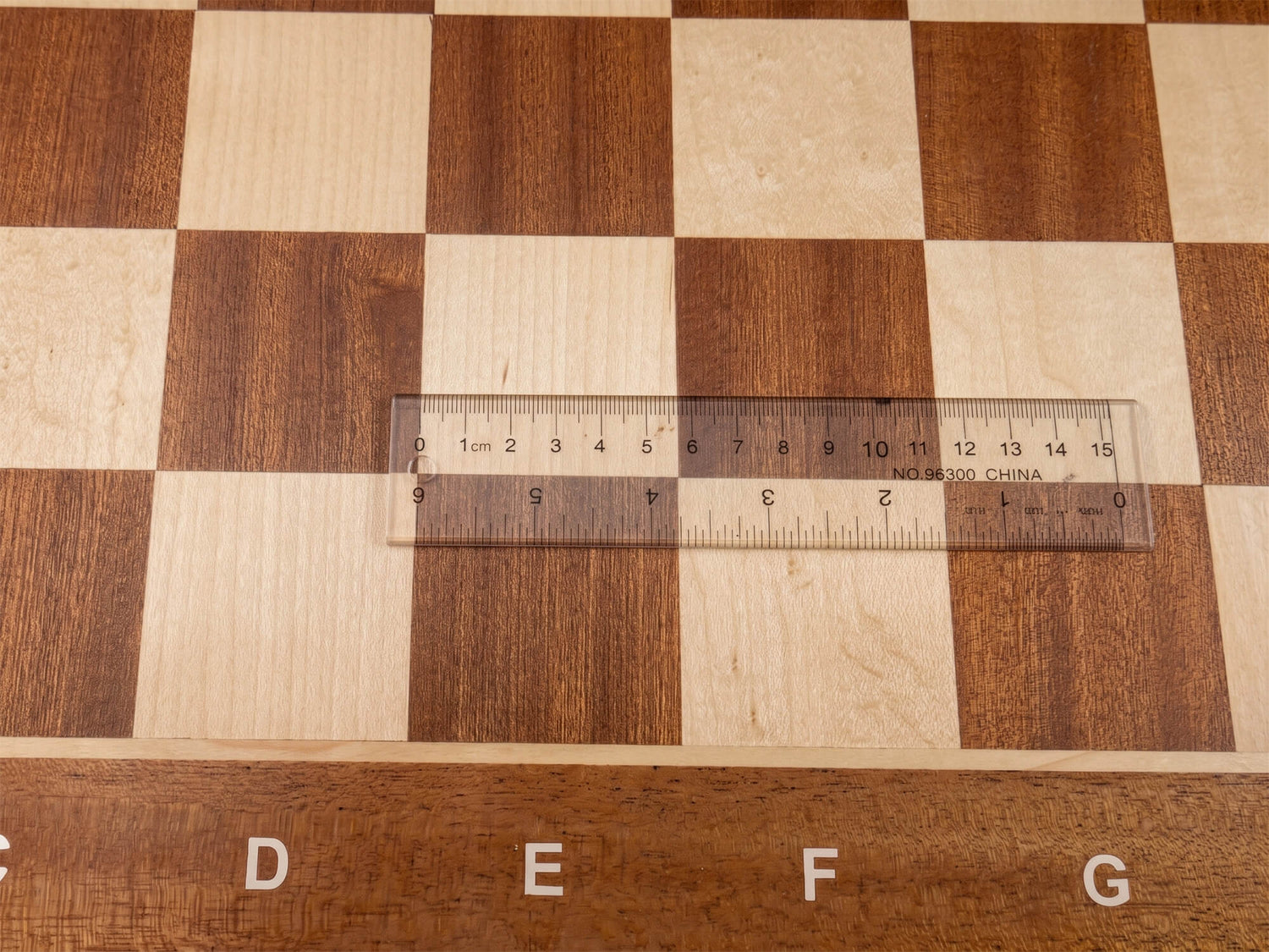 Close-up top view of the Monarch chess board with a transparent ruler placed across a square, confirming the precise 57mm regulation square measurement.