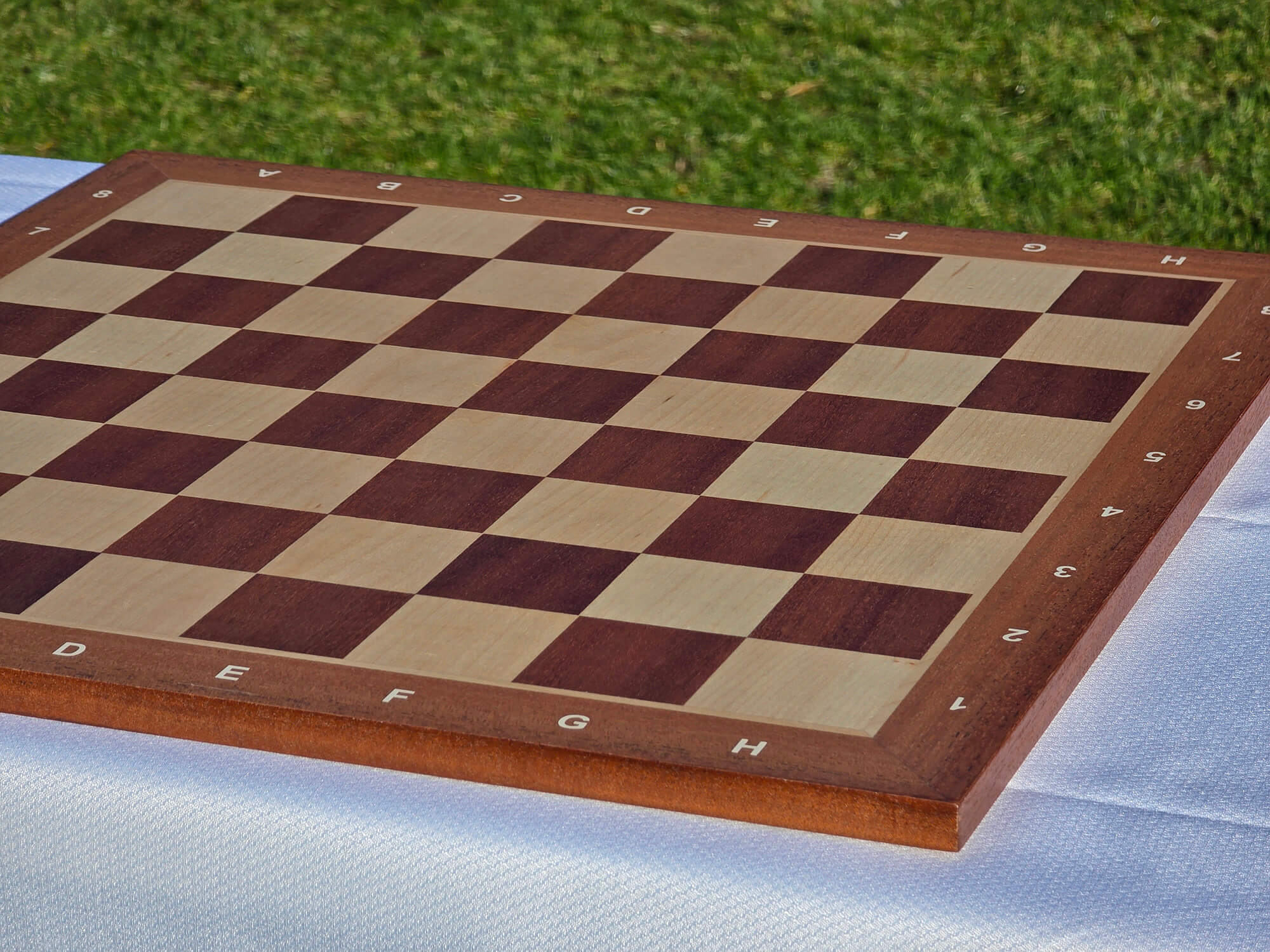 Side profile view of the premium Monarch wooden chess board on grass, highlighting the 15mm thickness and robust maple frame construction.