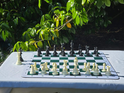 Wide angle shot of a green and white mousepad chess board with plastic tournament pieces arranged in the starting position outdoors.